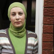 Woman in headscarf standing at the door of her house